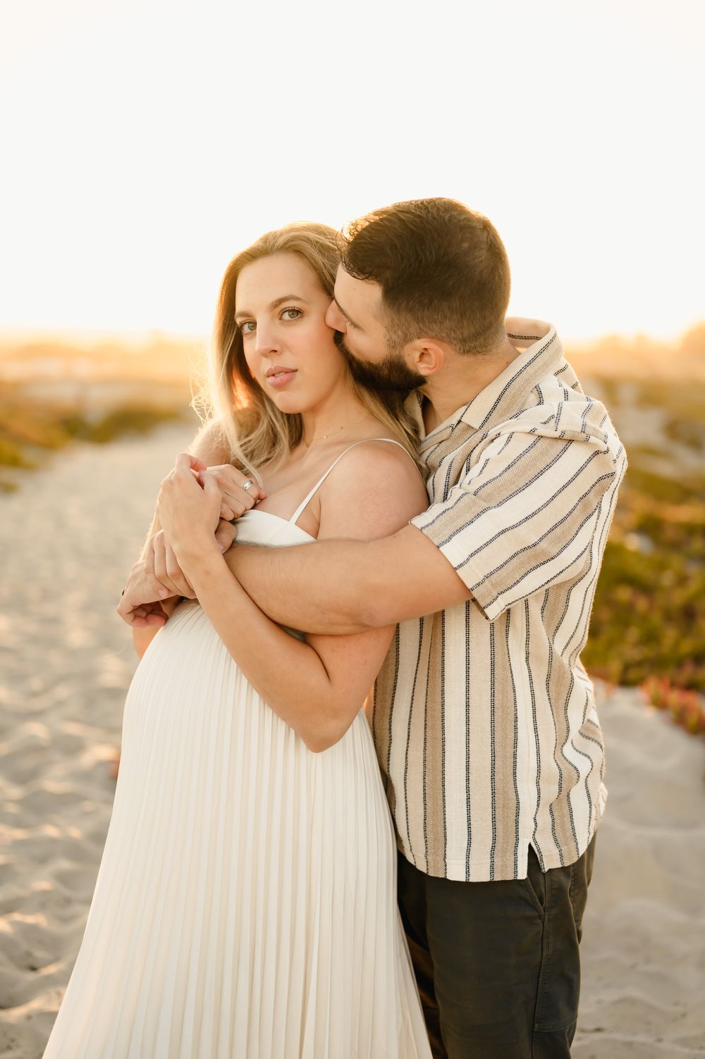 husband hugs wife from behind surrounded by golden sunlight during their maternity photoshoot by Ventura and Santa Barbara photographer