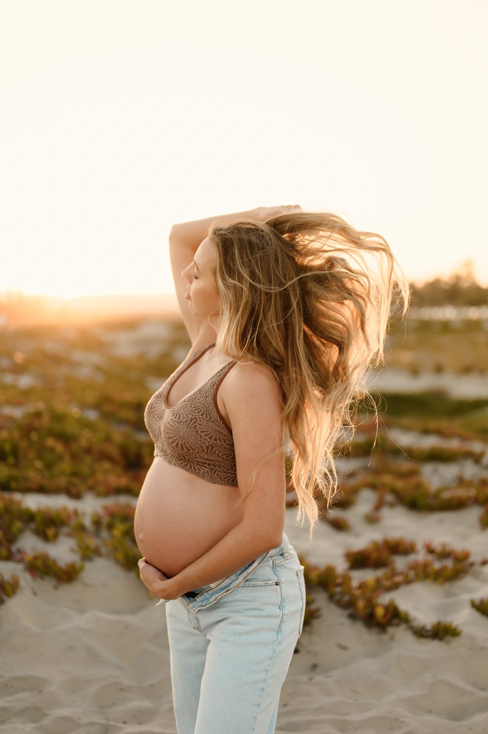 woman flips her hair highlighted by golden sunlight during her maternity photoshoot by Ventura and Santa Barbara photographer