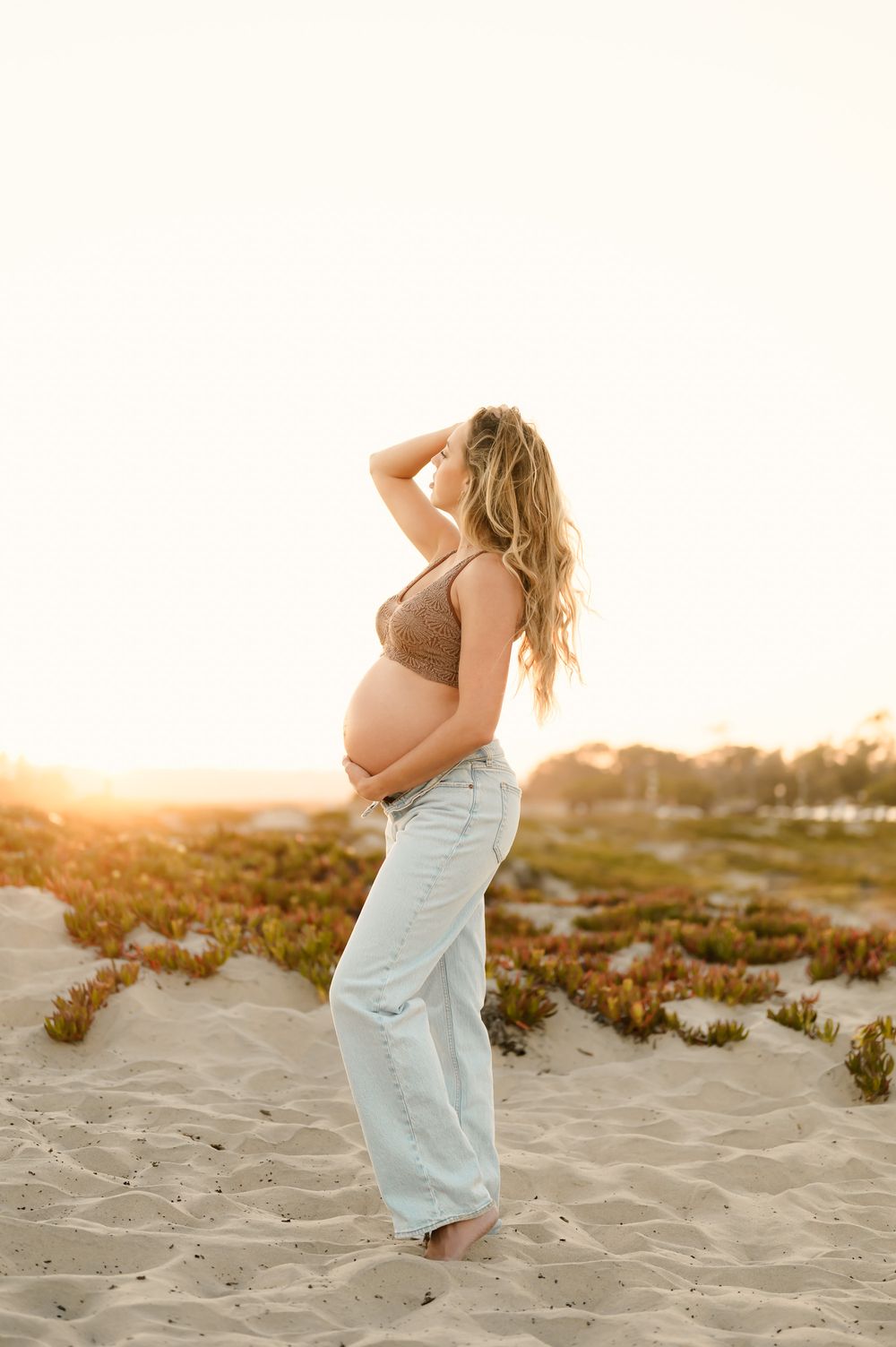 woman poses on sand dunes surrounded by golden sunlight during her maternity photoshoot by Ventura and Santa Barbara photographer