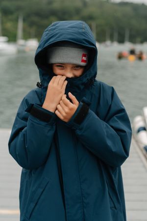 Someone in a navy blue raincoat with hood pulled up covering their mouth on a rainy day.