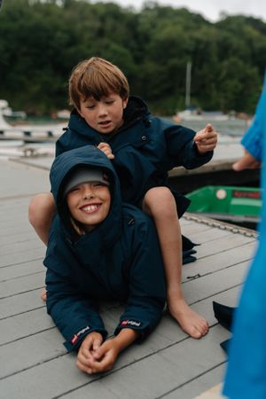 Two people in matching blue coats playing on a wooden dock near boats.