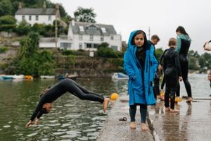 People in raincoats stand on a wet dock while someone dives into the water.