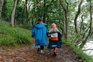 Two people walking along a wooded forest path wearing raincoats on a misty day.