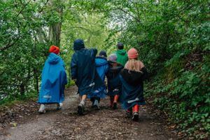 Group of children in blue coats walking along a wooded path together.