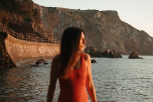 A silhouette stands at a coastal cliff edge during golden hour with rugged rock formations and ocean waves below.