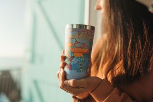 Someone holds a colorful decorated drink can against a soft sunlit background.