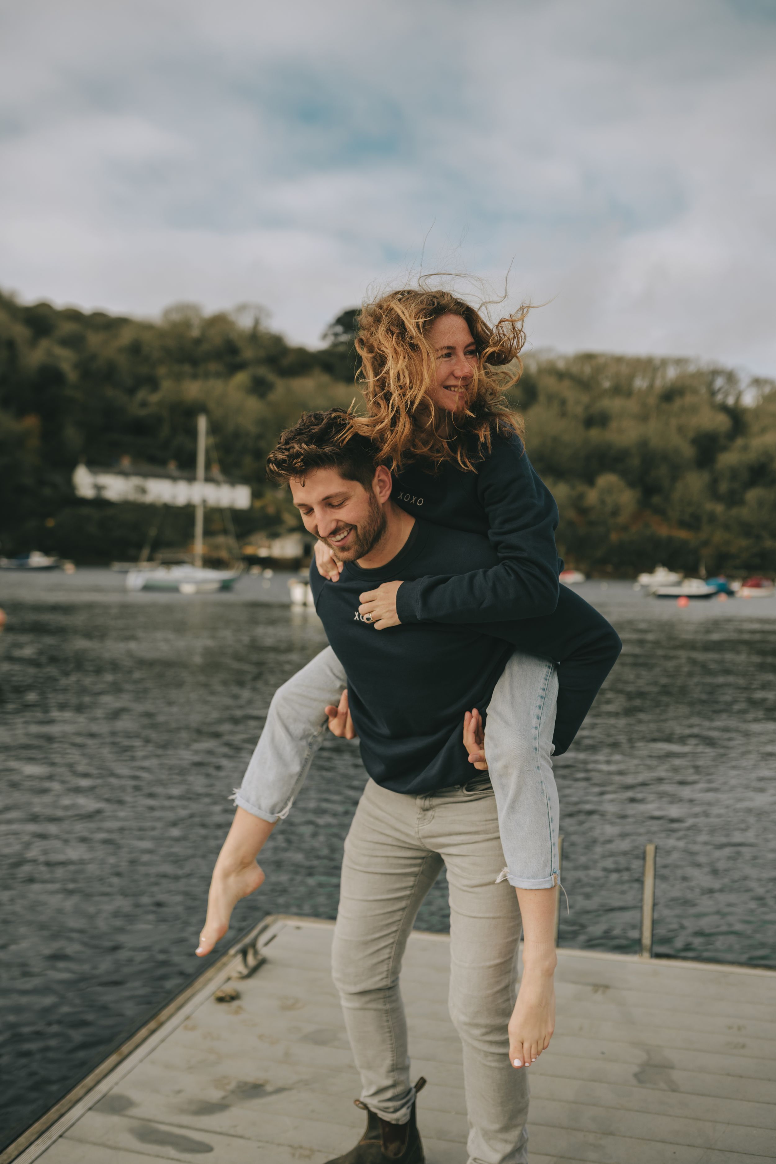 Playful piggyback ride on wooden dock with boats and water in background.