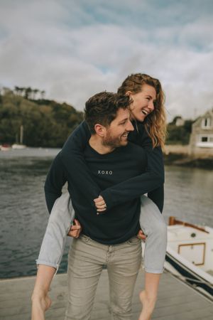 Couple sharing joyful piggyback moment on dock by waterfront.
