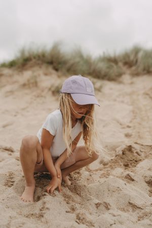 A young figure in a baseball cap crouches down to explore the sandy beach.  Branding photography, Devon