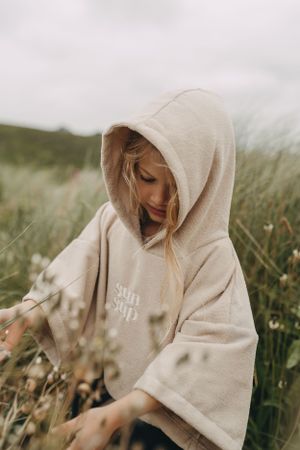 Person wearing a beige hoodie amid tall grass on a cloudy day.