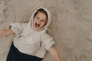 Joyful moment captured of someone laying on sandy ground in a beige hoodie.  Branding photography, Devon