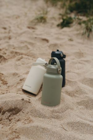 Three minimalist water bottles in neutral colors placed on sandy beach. Branding photography, Devon