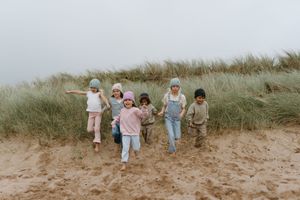 Kids running together on a sandy beach path near tall grass in misty weather.