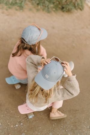 Two skateboarders in matching outfits and light blue baseball caps crouching on a dirt path with pink and blue decks.