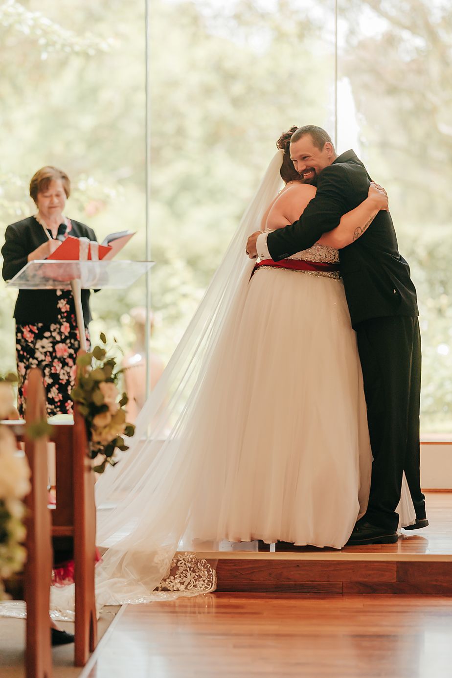 Heartfelt embrace during wedding ceremony in chapel with floral decor and evening light streaming through windows.