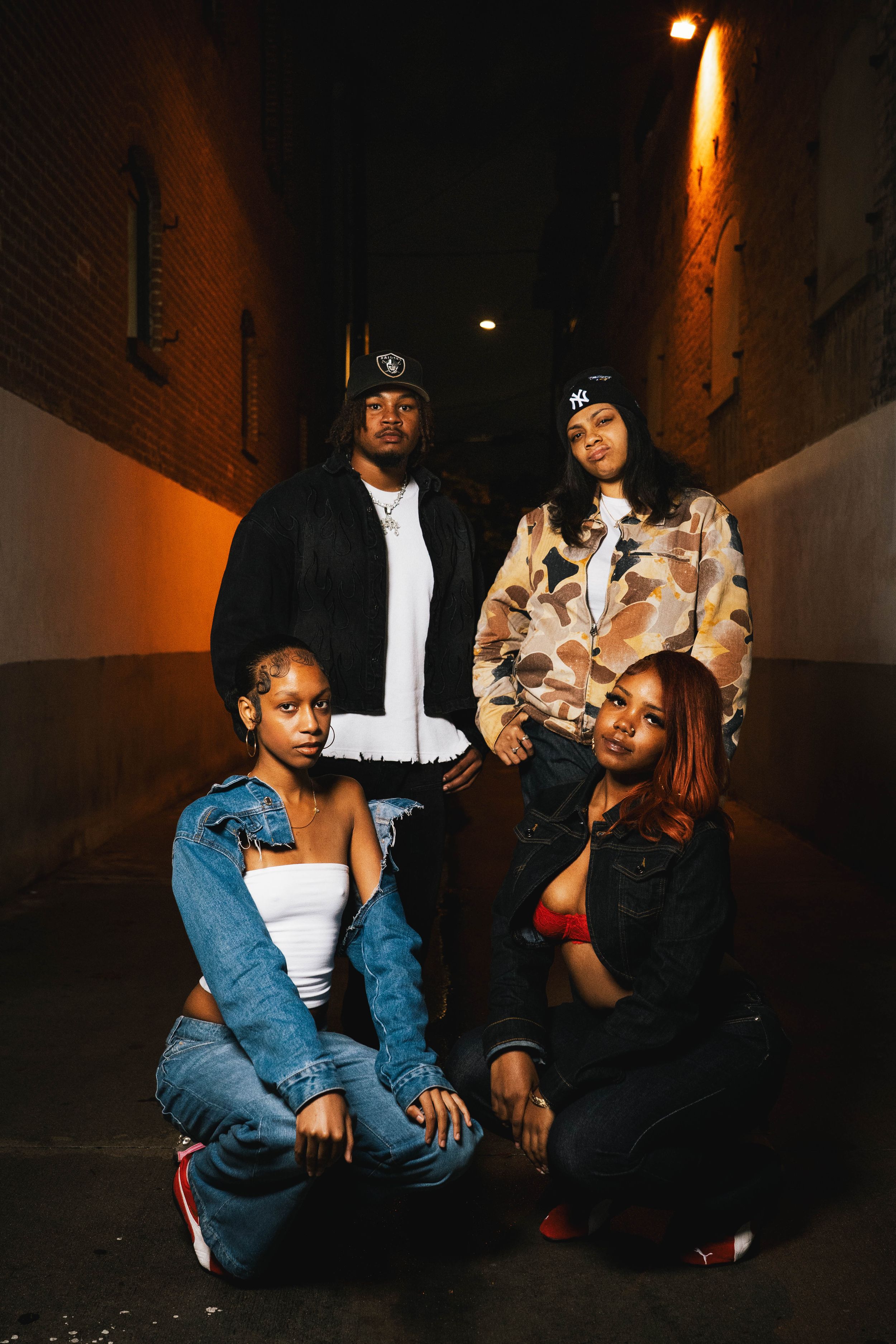 Group of friends sitting in a dimly lit alley with warm lighting and brick walls in an urban nighttime setting.