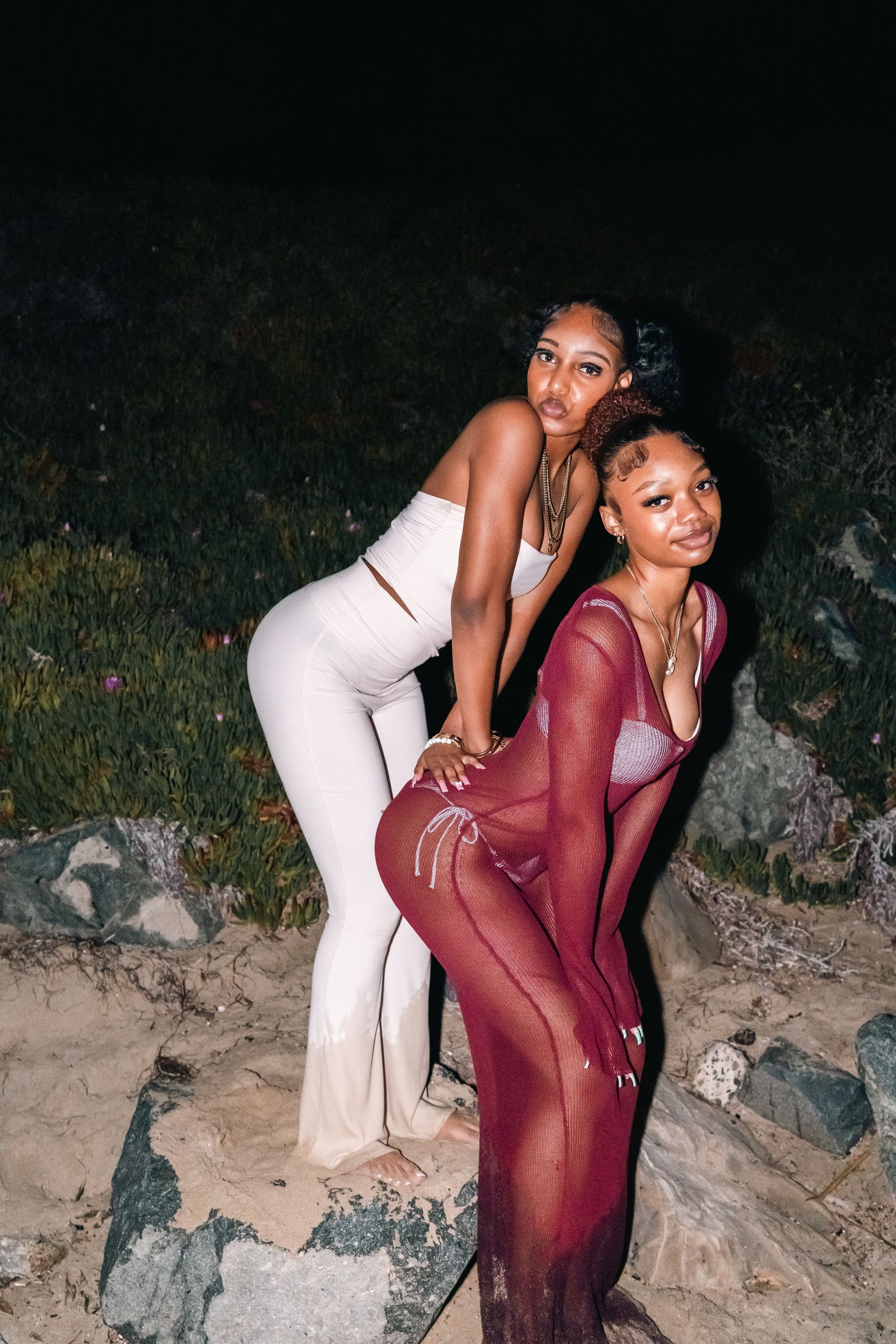 Two friends pose together on rocks, wearing white and burgundy evening outfits.