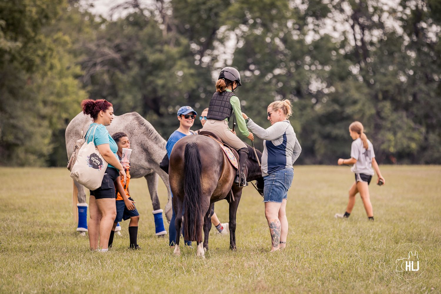 Athletic group performs stretching exercises on grass field with horses during outdoor fitness class.