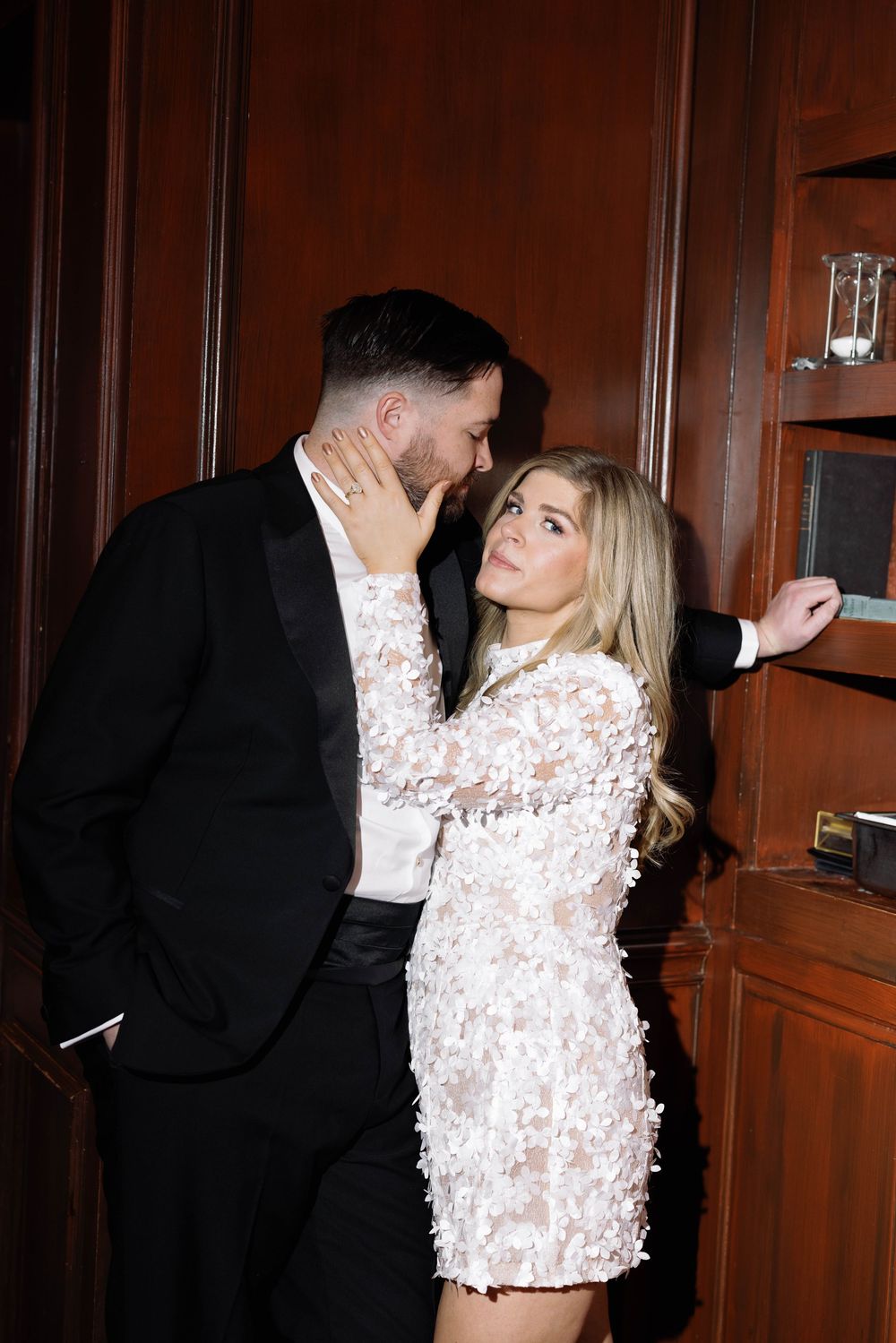 Couple in formal attire sharing romantic moments against wooden paneled wall.