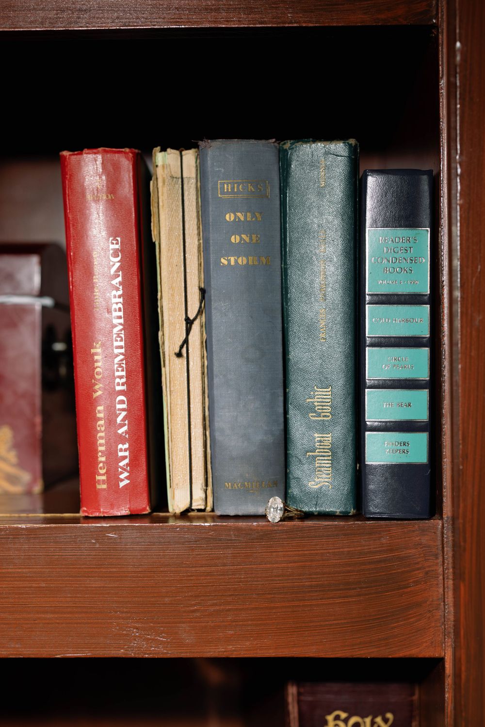 Old vintage books with worn spines arranged on a dark wooden shelf.