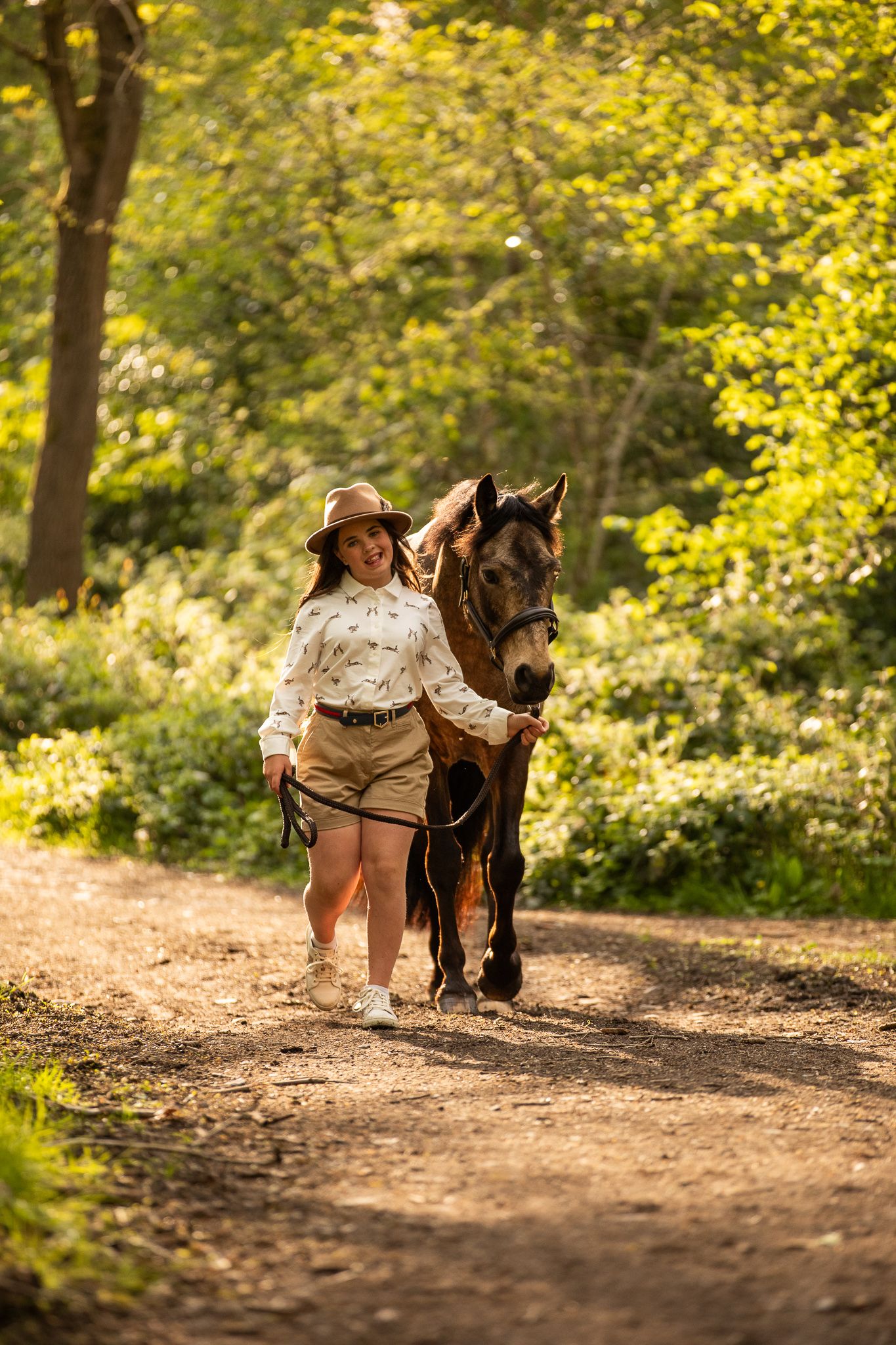 A large cream-colored draft horse and its companion pause together in a sunlit autumn forest.