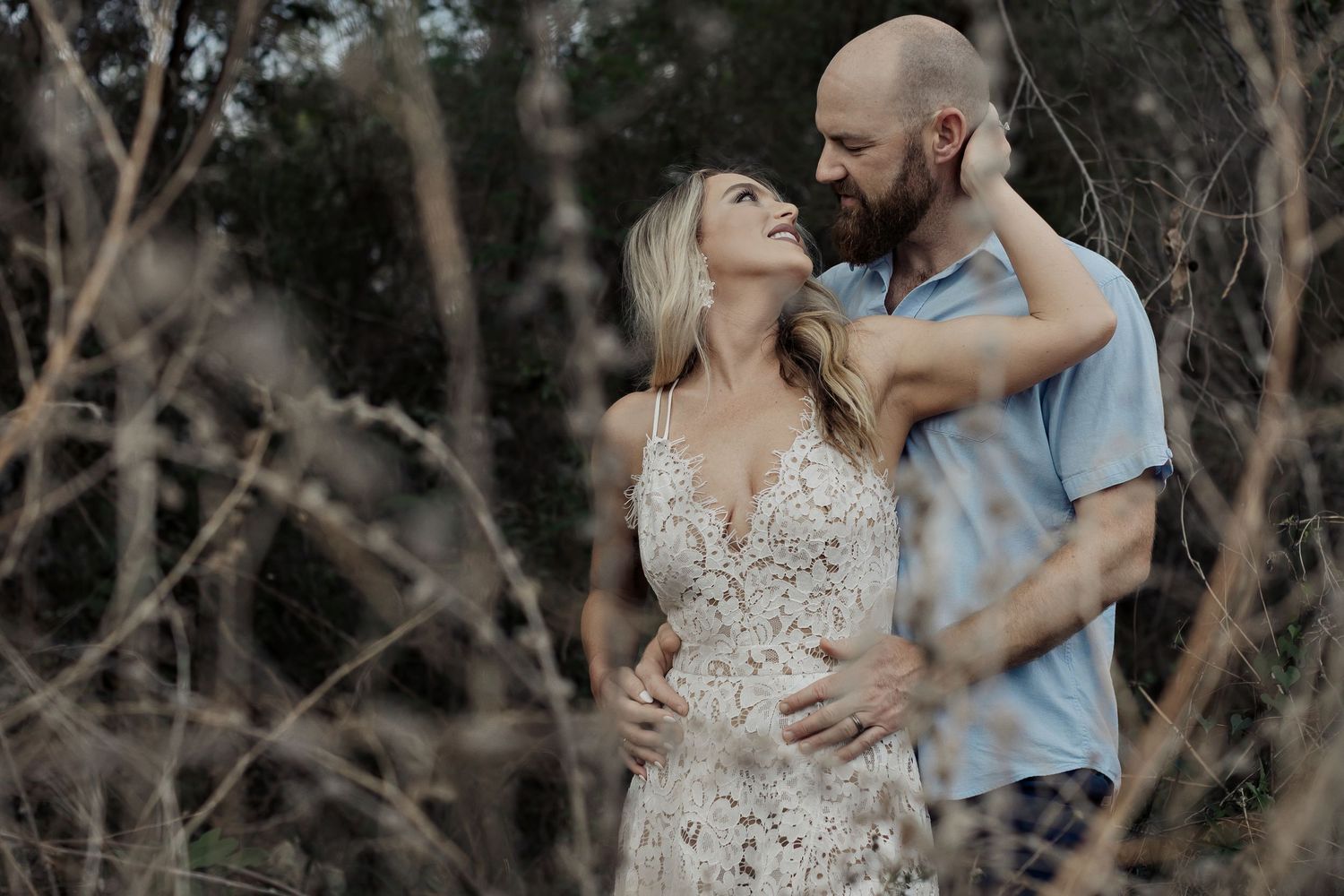 A romantic couple embraces outdoors during an engagement photoshoot in a rustic wooded setting.