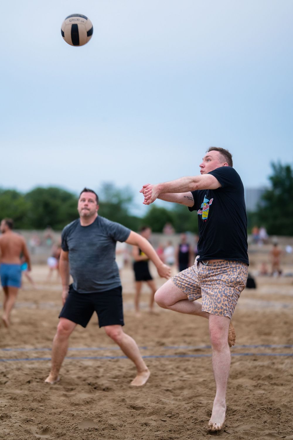 An athlete on the beach lines up a bump to return the ball over the volleyball net while his teammate looks on