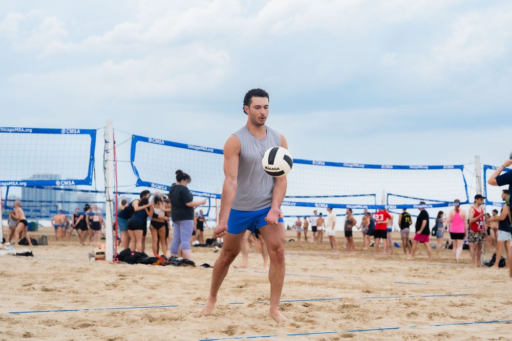 An athlete serves the volleyball on the beach to start the point