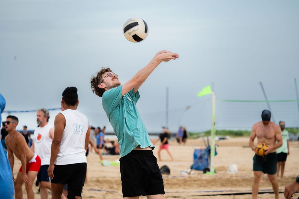 An athlete on the beach lines up a bump to return the ball over the volleyball net