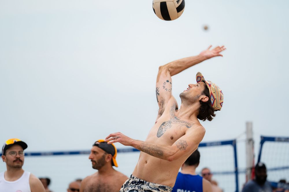 An athlete on the beach lines up a bump to return the ball over the volleyball net