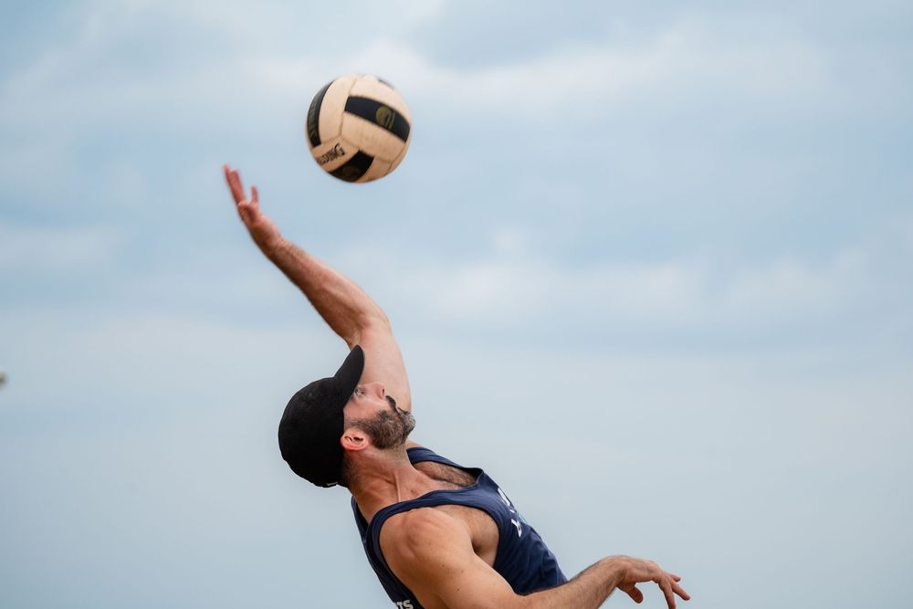 An athlete on the beach lines up a bump to return the ball over the volleyball net