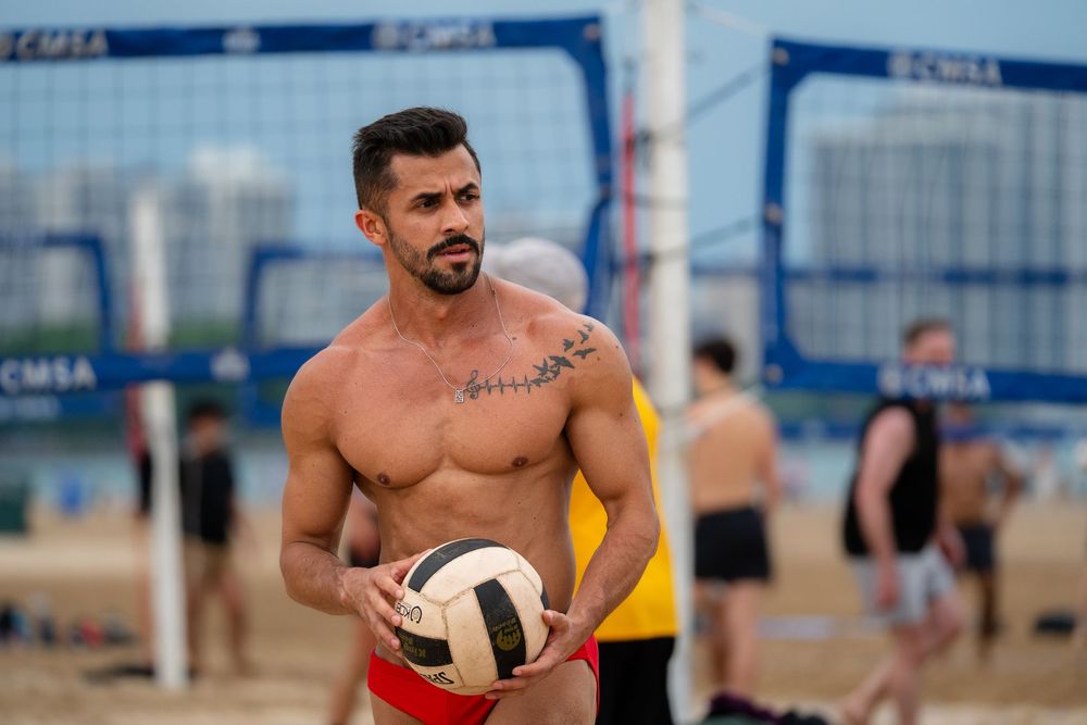 An athlete waits with the volleyball in hand to start the serve on the beach