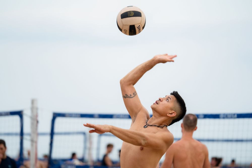 An athlete on the beach lines up a bump to return the ball over the volleyball net