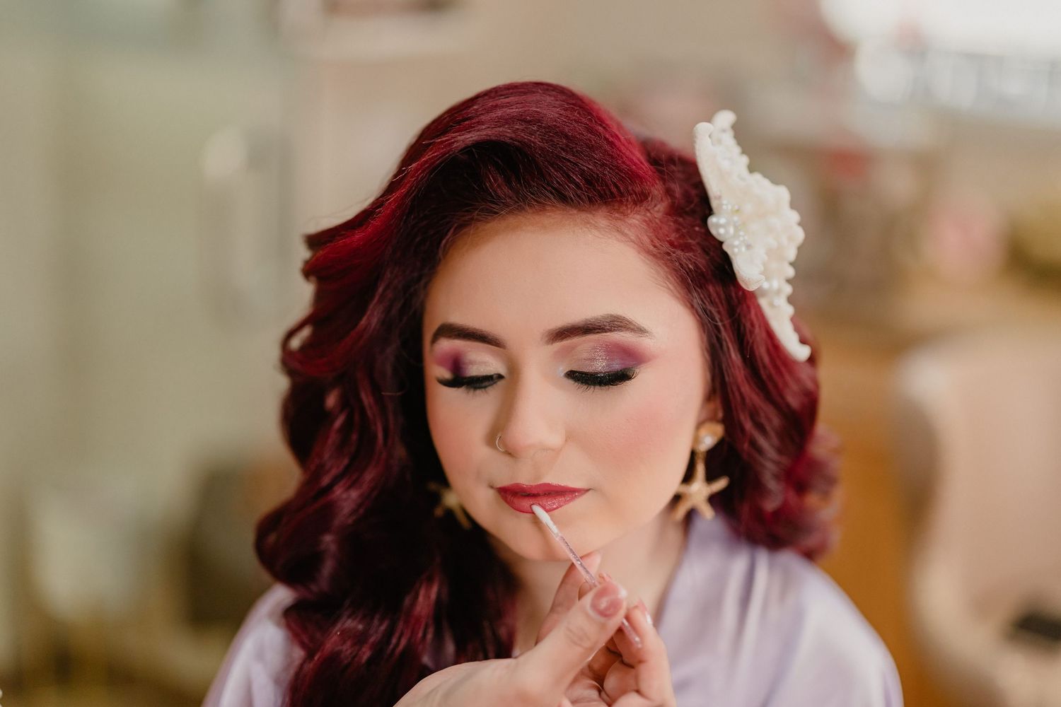 Quinceanera wearing burgundy red hair, smoky eye makeup, and delicate white floral hair accessories poses for wedding photos.