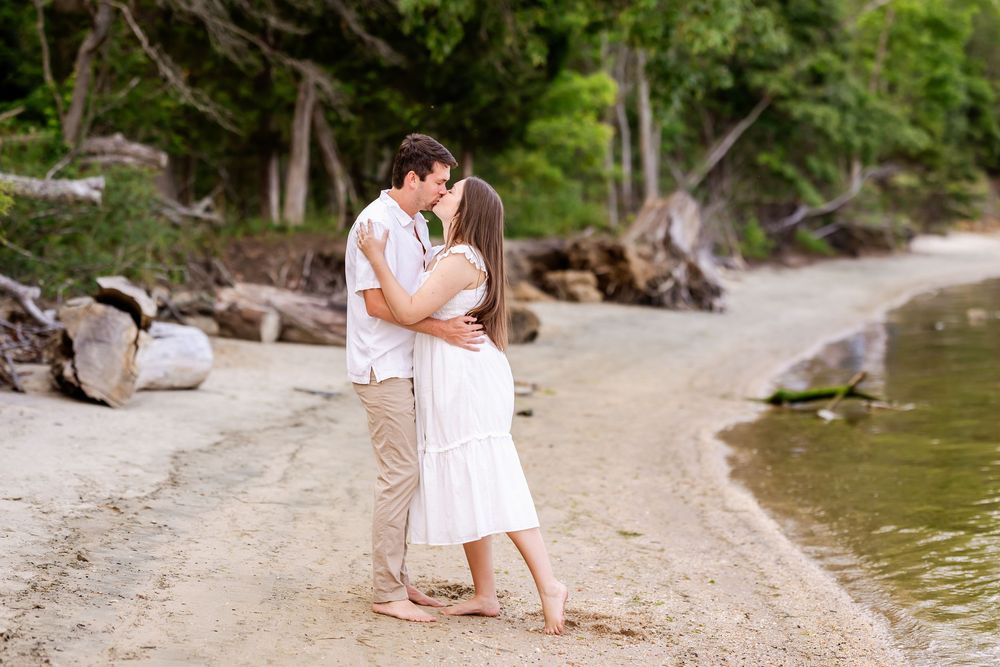 Couple in white outfits shares romantic moment on sandy beach at sunset.