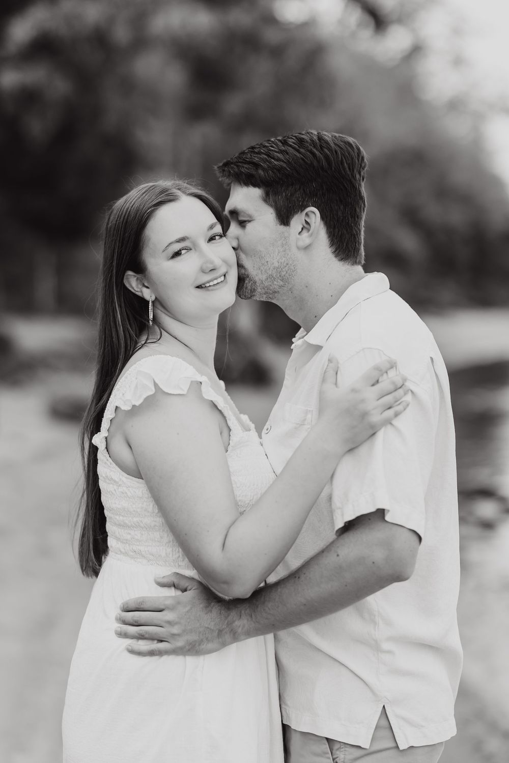 A romantic black and white portrait of a loving couple embracing outdoors in soft natural lighting.