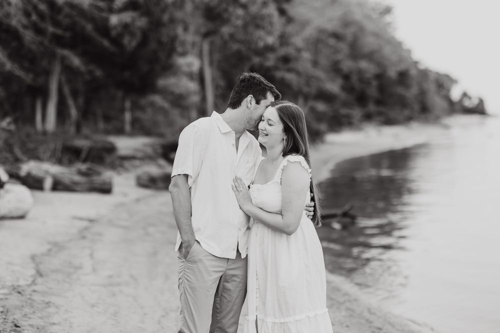 A couple stands close together in an intimate moment on a beach shore in black and white photography.