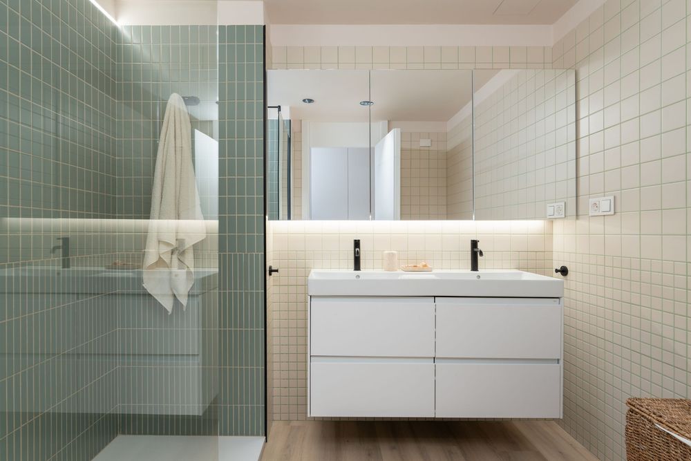 Modern bathroom interior with white floating vanity, green tiled shower partition, and sleek minimalist design.