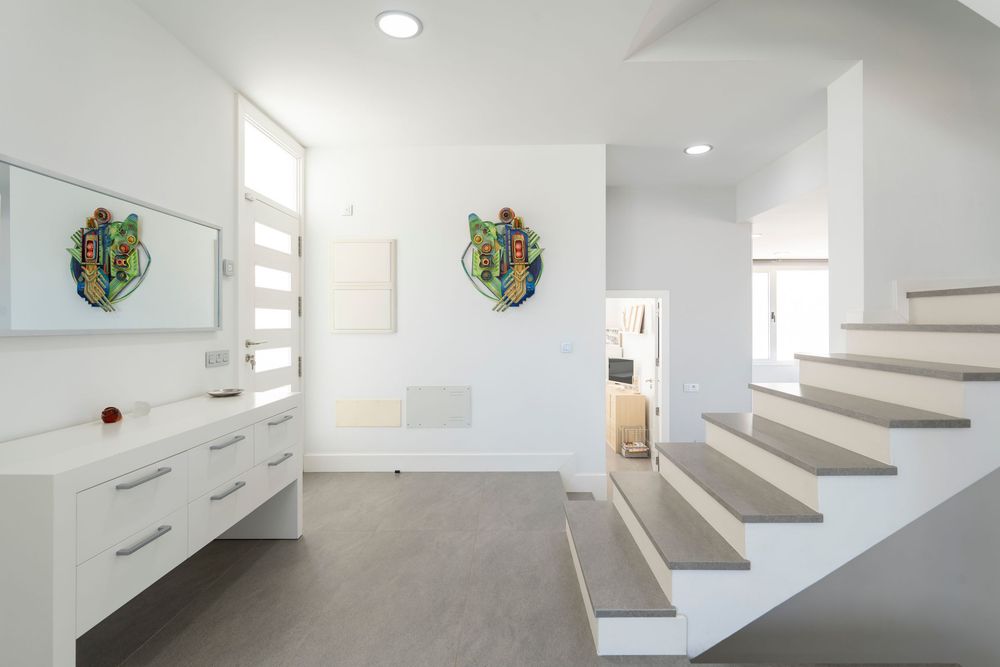 Bright modern interior hallway featuring white walls, floating stairs, and colorful wall art with built-in storage.