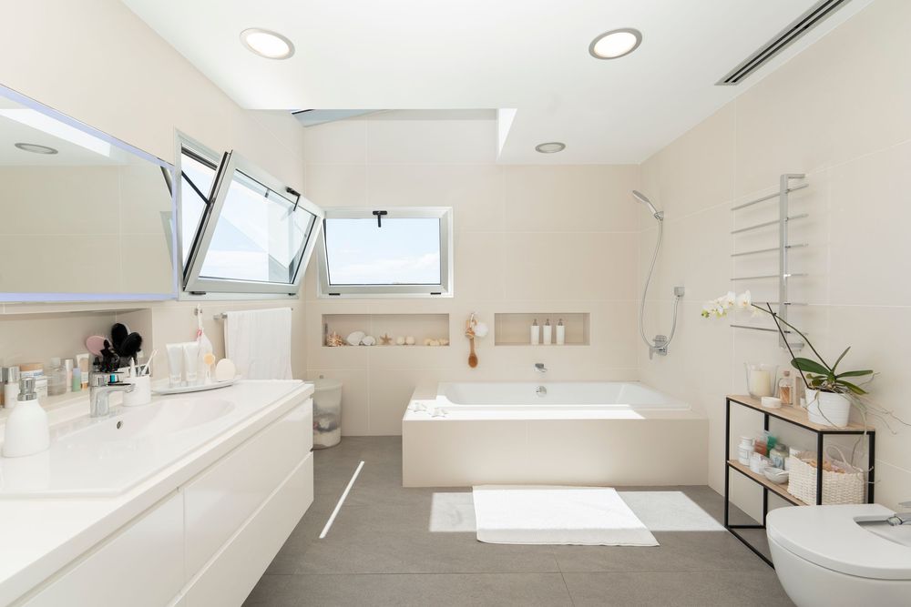 Modern white bathroom with skylight features floating vanity, freestanding tub and gray tile floors in minimalist design.