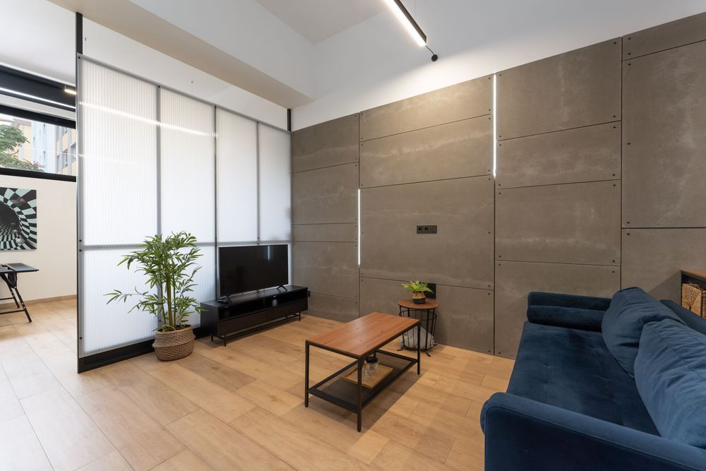 Contemporary living room with blue sofa, coffee table and concrete accent wall illuminated by natural light.