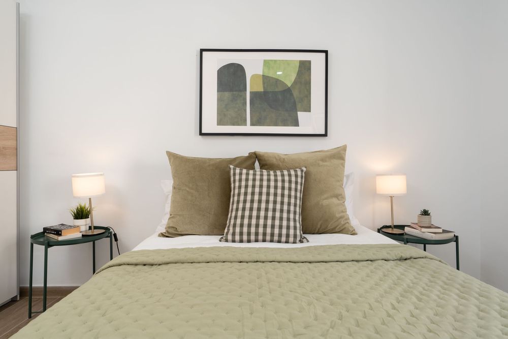 Contemporary bedroom interior with olive green throw pillows, framed wall art, and clean white bedding.