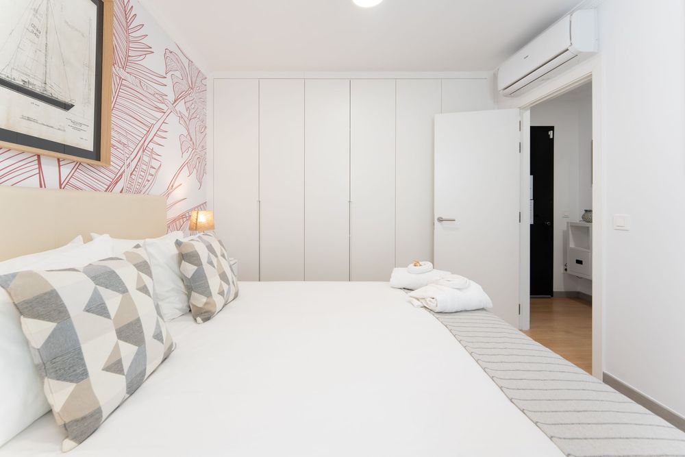 Modern white bedroom interior with geometric pillows and minimalist decor on white paneled walls.
