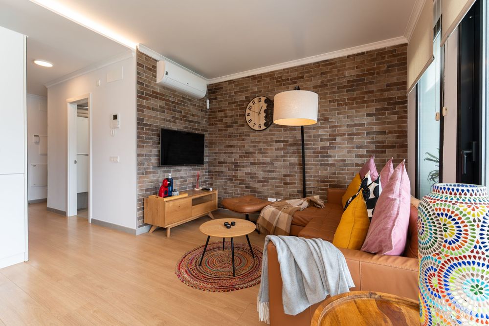 A modern open-concept living room features exposed brick walls, hardwood floors, and contemporary furnishings in warm tones.