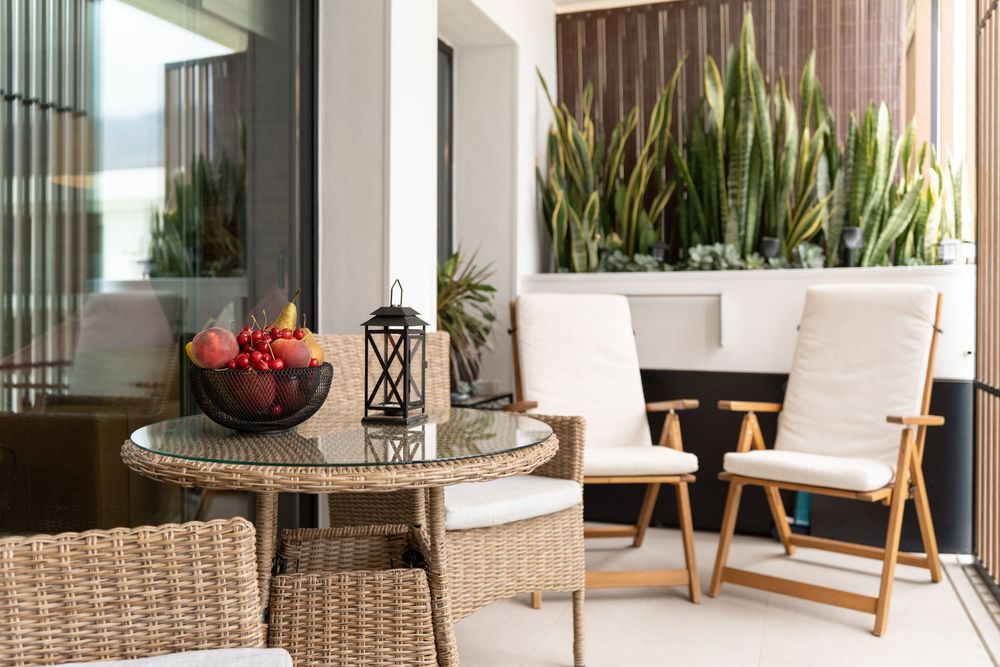 Modern patio furniture with woven coffee table, decorative lantern, and potted snake plants against a white exterior wall.