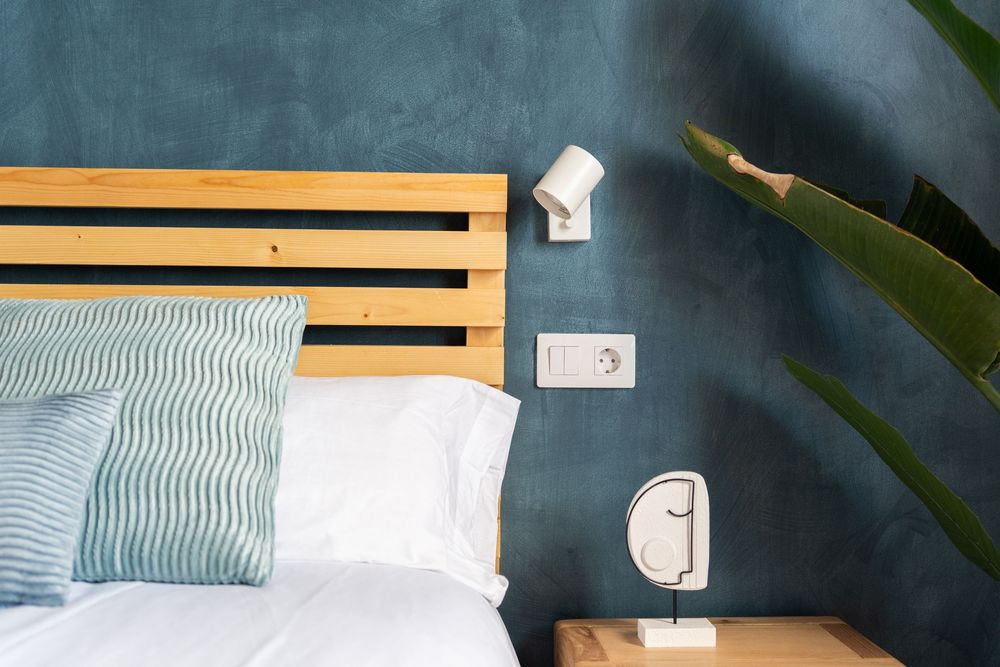 Modern bedroom interior with light wood headboard and blue striped bedding against dark navy accent wall.