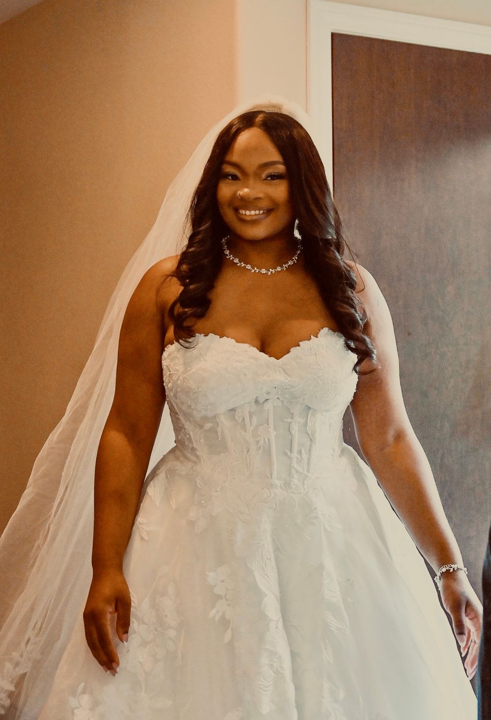 Beautiful Black bride smiling in strapless lace wedding gown with veil and diamond necklace.