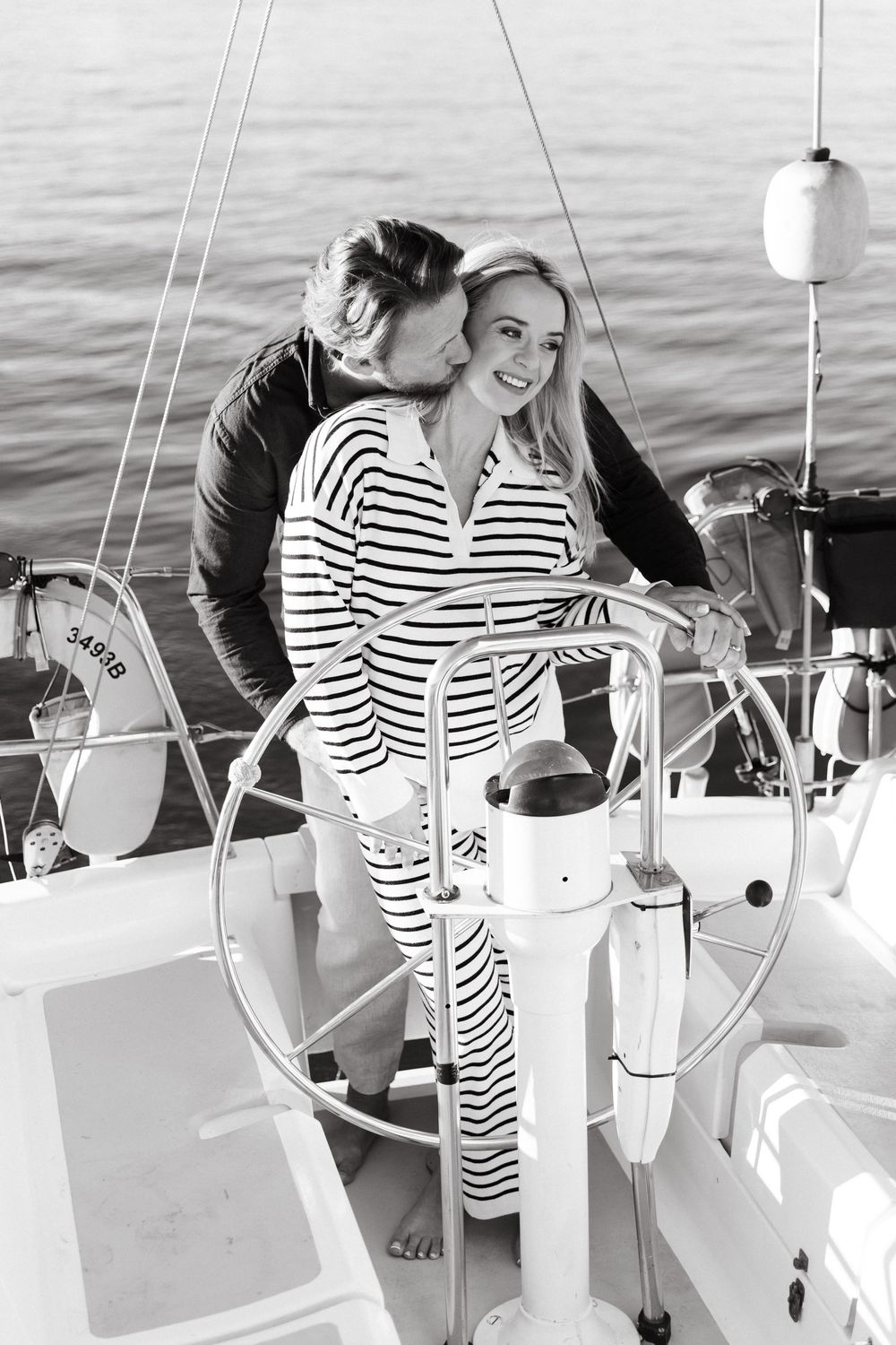 Black and white photo of a couple sharing an intimate moment while sailing on a boat at sea.