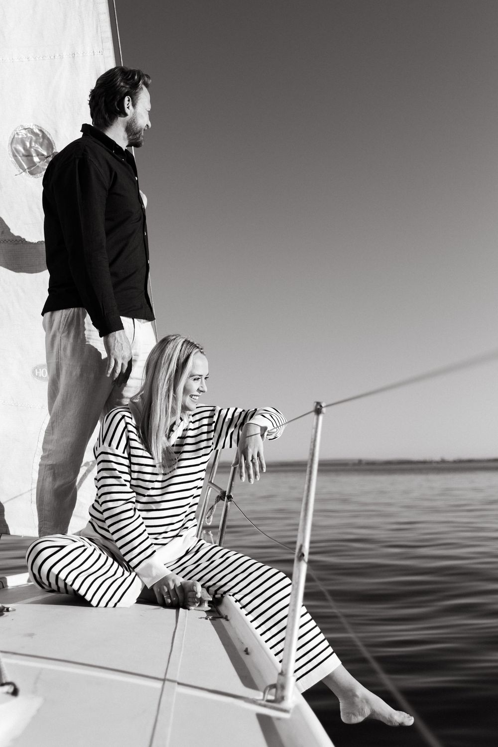 A couple enjoys a peaceful moment on a sailboat with one person wearing a striped nautical outfit.