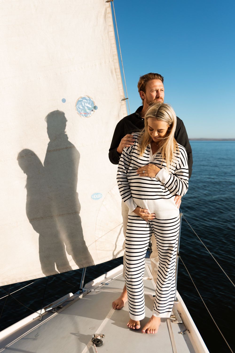 Couple in matching striped outfits standing on a sailboat deck against blue ocean and sky backdrop.